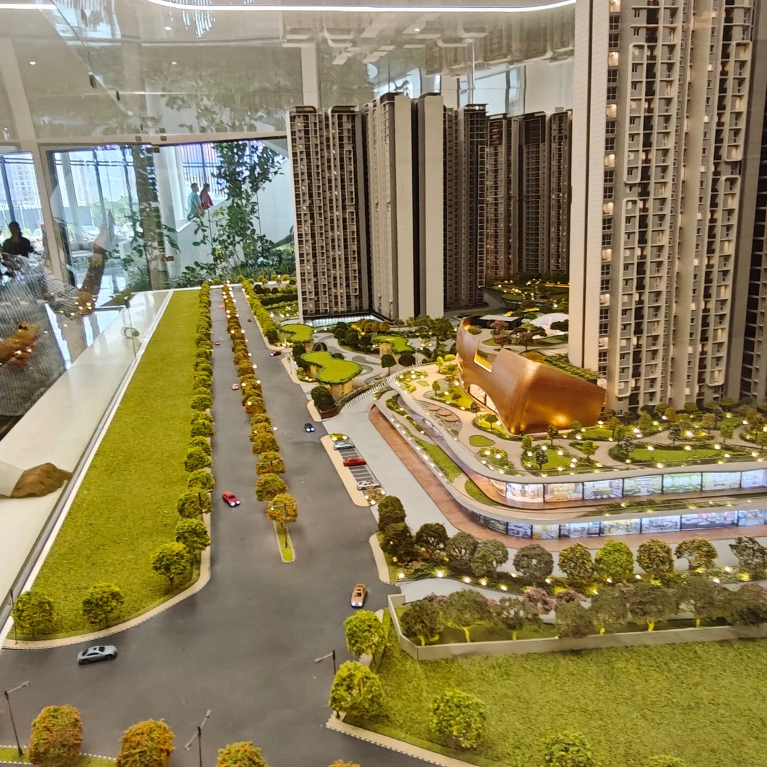 High-angle scale model observation of the main approach avenue, showing the tree-lined road leading towards the residential towers and clubhouse