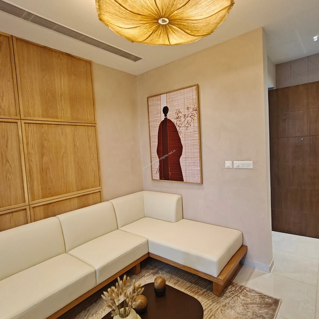 Interior view of the 2 BHK show flat living room at Purva Northern Lights featuring a cream sectional sofa, light wood wall paneling, and an organic fabric pendant light