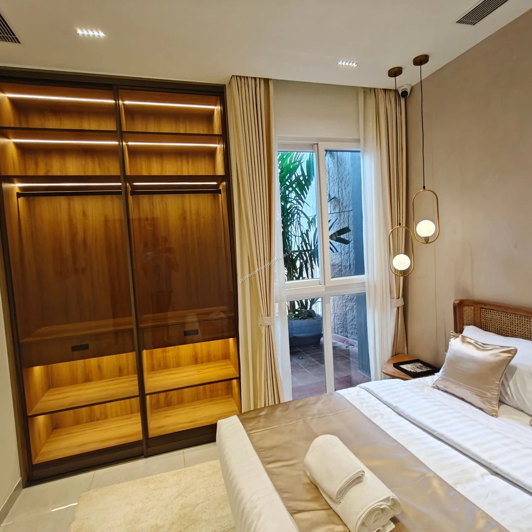 Master bedroom at Purva Northern Lights showcasing a designer wooden wardrobe with integrated LED lighting and a cane-textured headboard