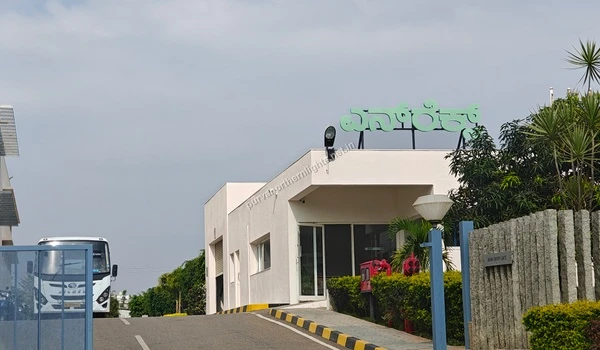 Main entrance gate and security building of Enercon India Pvt. Ltd. with a white bus passing through near Purva Northern Lights