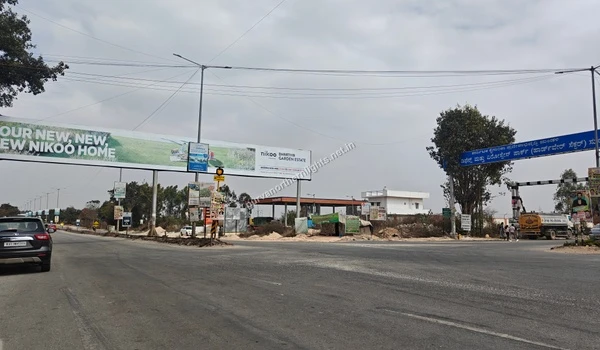 Wide road intersection with Nikoo Homes billboard and traffic near Purva Northern Lights