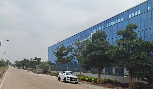 Street view perspective of the long RTX building with blue glass windows and a white car driving on the road near Purva Northern Lights