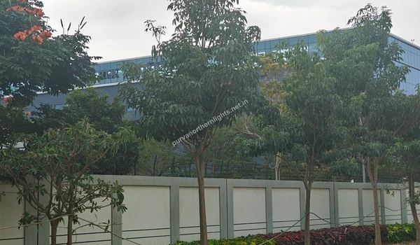 View of the RTX building partially hidden behind dense green trees and garden landscaping near Purva Northern Lights