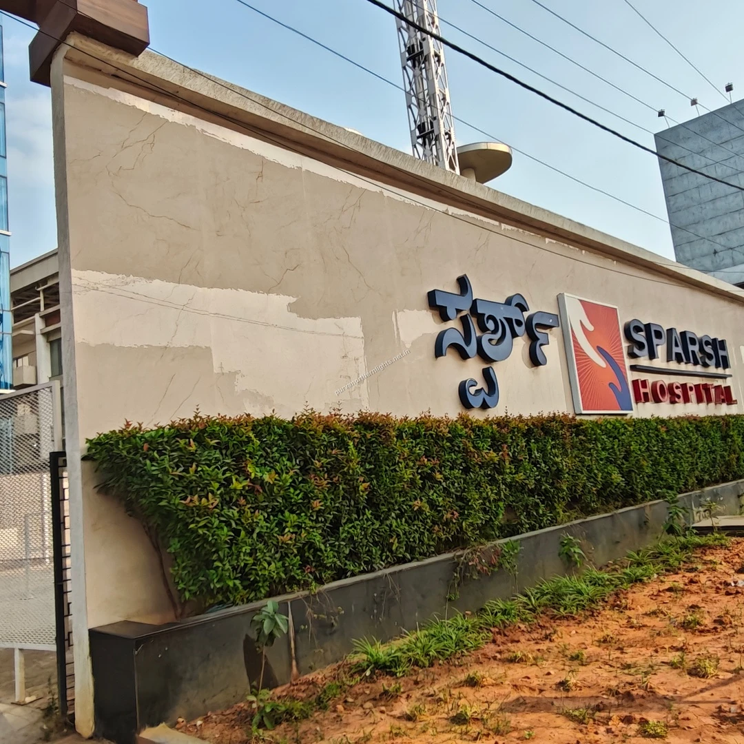 Side angle of the Sparsh Hospital boundary wall featuring regional Kannada lettering conveniently located near the Purva Northern Lights project.