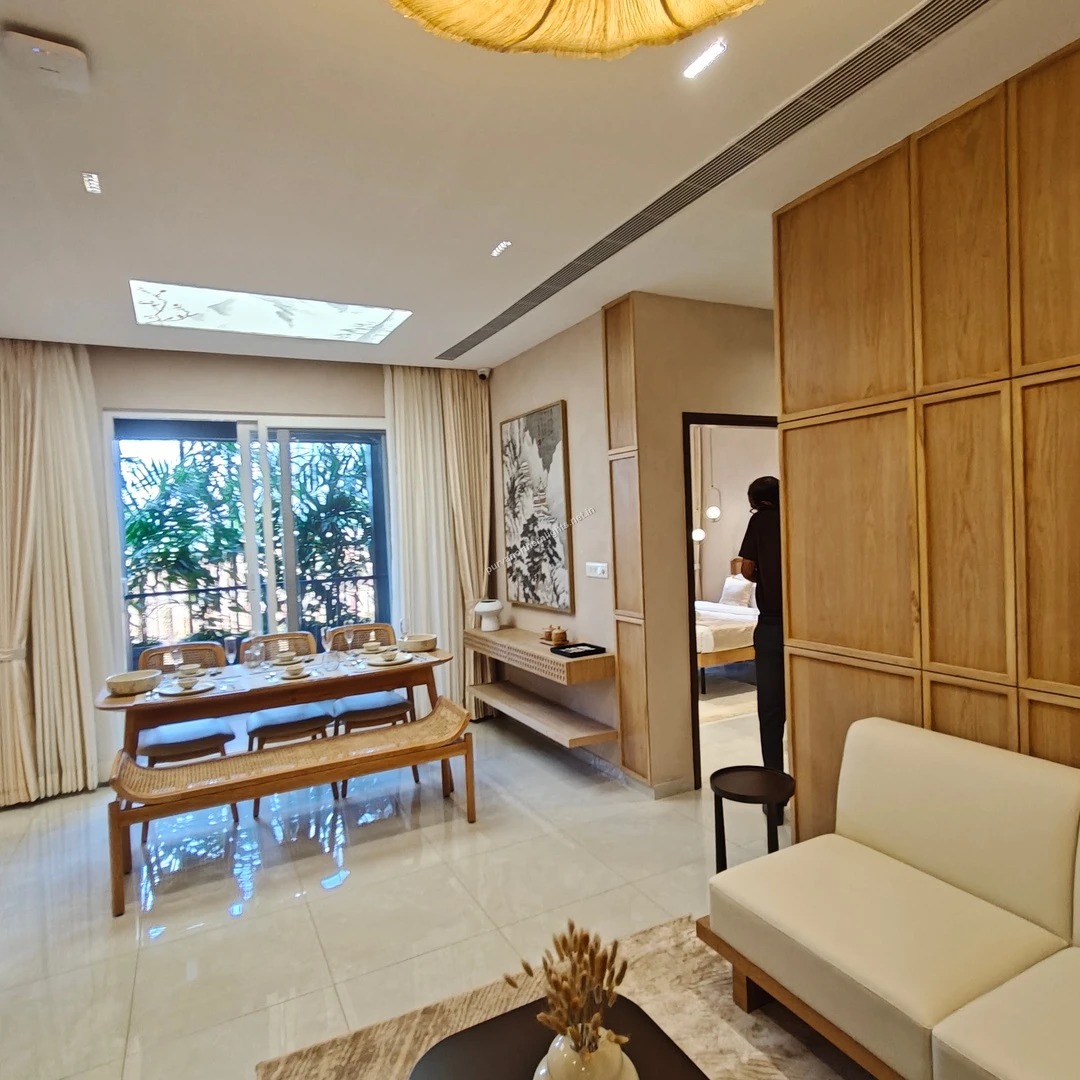 Open-concept dining area at Purva Northern Lights with a wooden table, rattan bench, and large floor-to-ceiling windows overlooking the balcony greenery